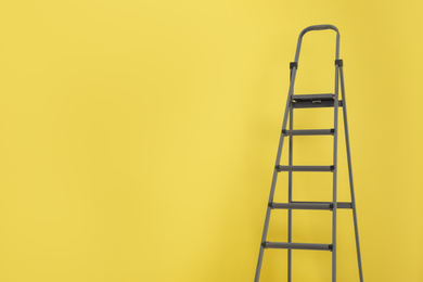 Metal stepladder on yellow background. Space for text
