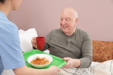 Nurse giving tray with food to senior patient in hospital ward. Medical assisting