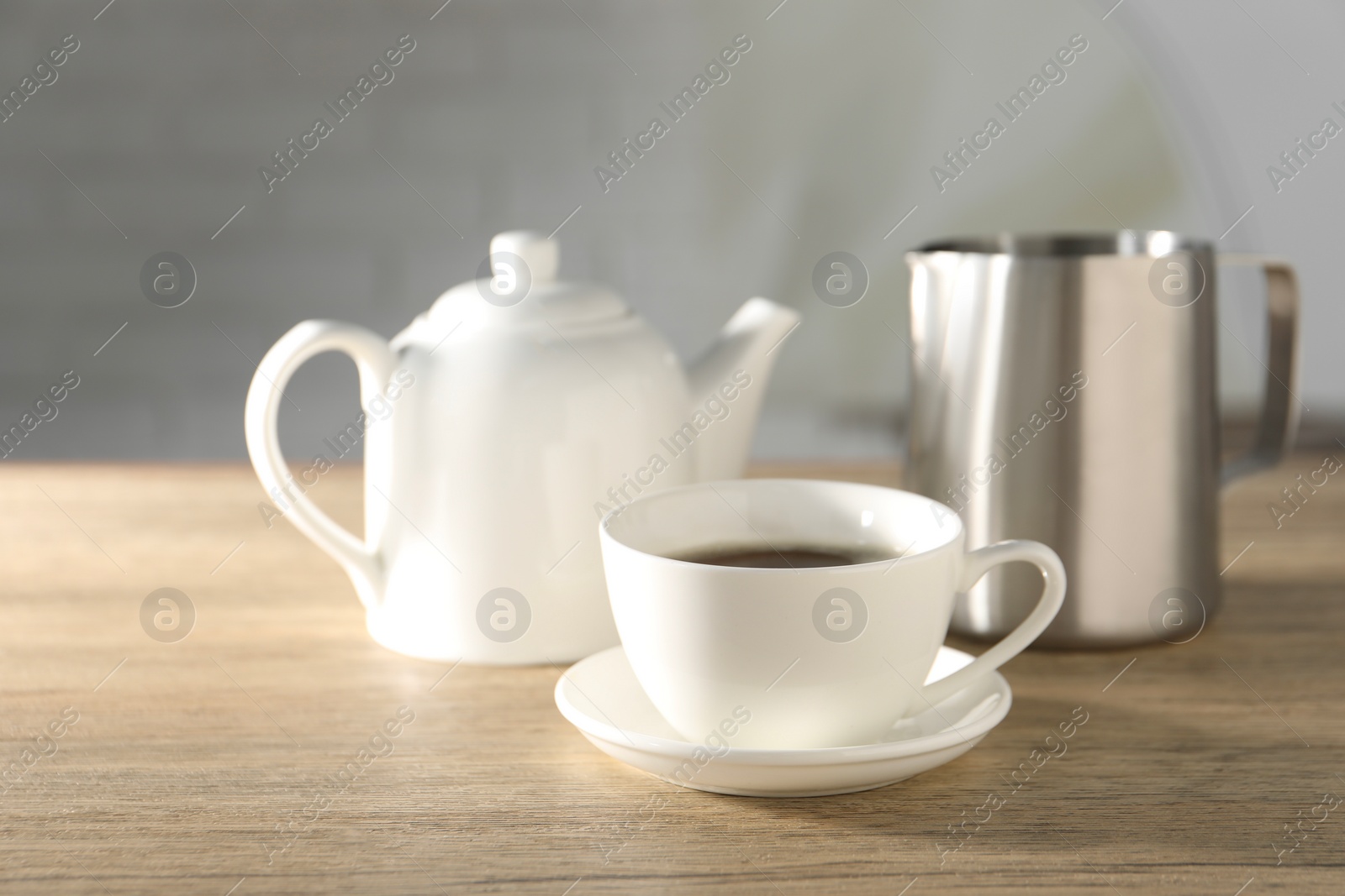 Photo of Aromatic tea in cup, teapot and pitcher on wooden table