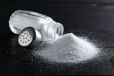 Photo of Organic salt in glass shaker on black wooden table, closeup