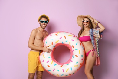 Photo of Young couple in beachwear with inflatable ring on color background