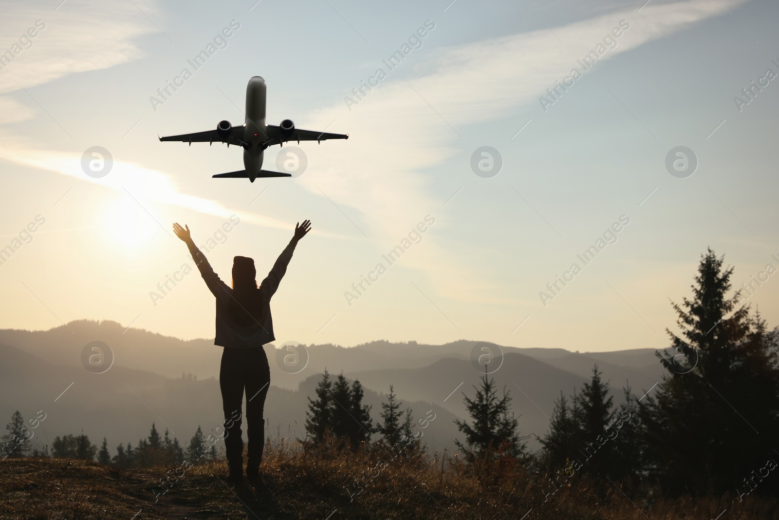 Image of Woman looking at airplane flying in sky over mountains, back view