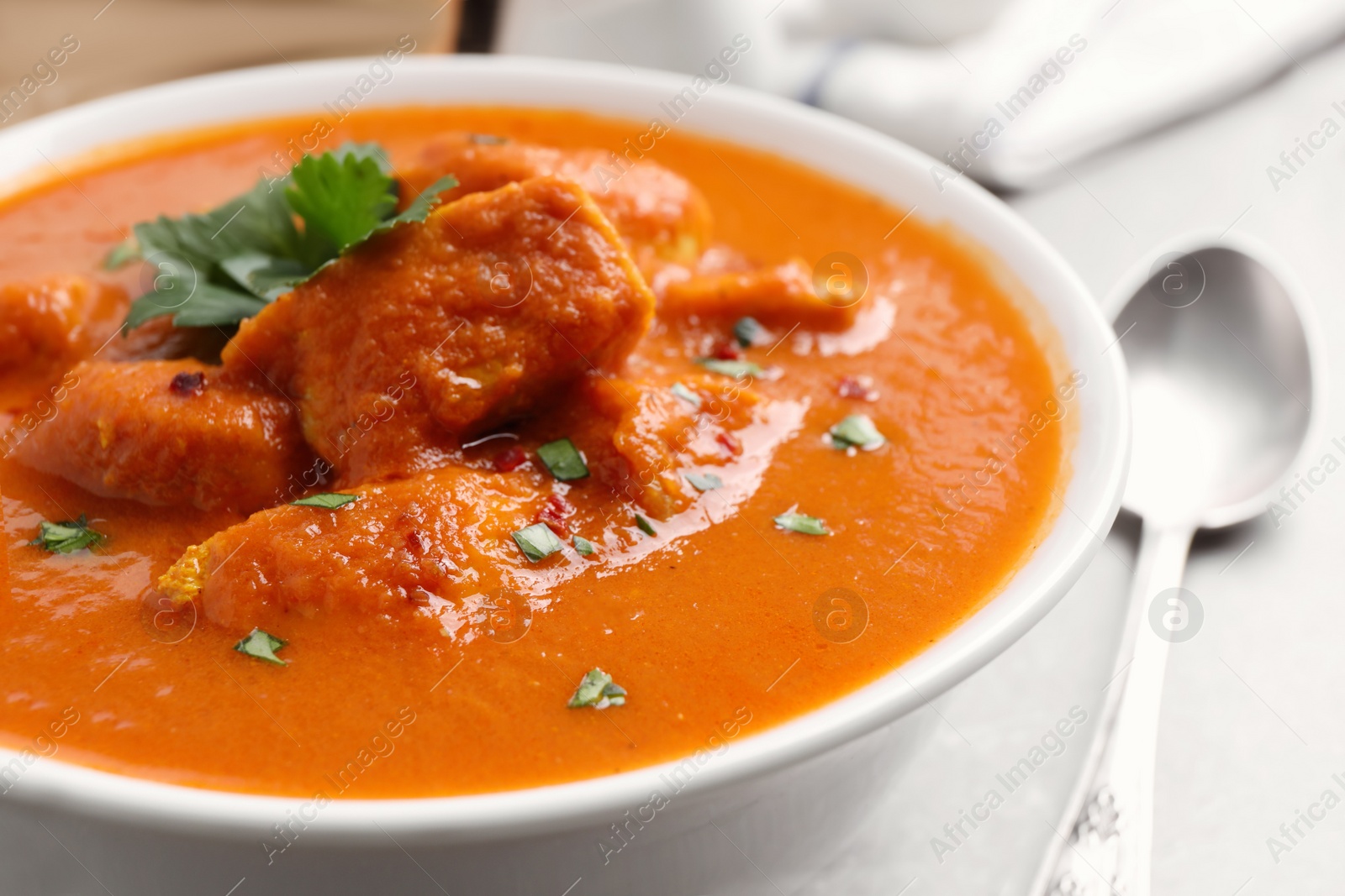 Photo of Bowl of delicious chicken curry on light grey table, closeup