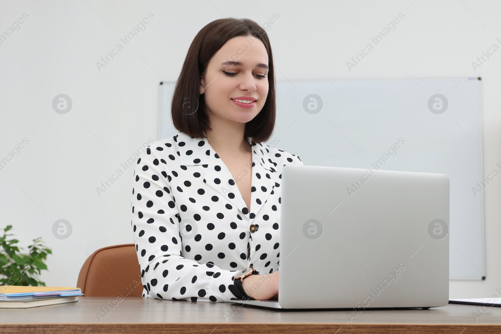 Photo of Happy young intern working with laptop at table in modern office