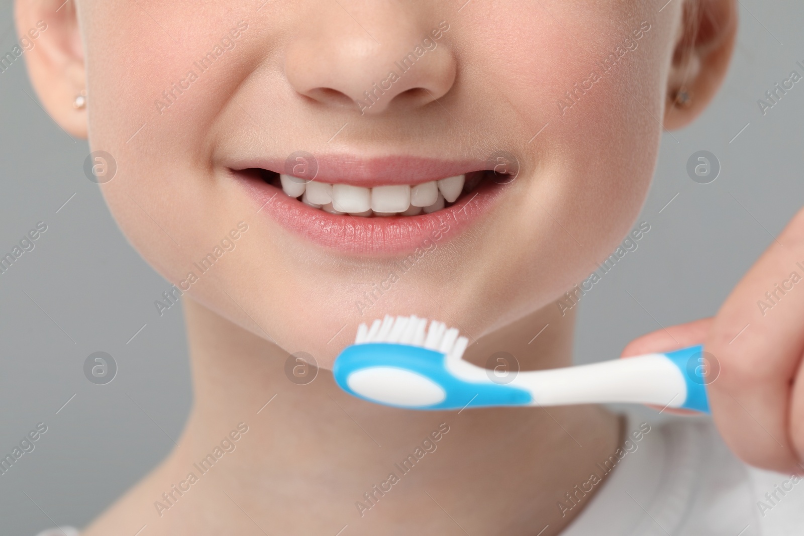 Photo of Girl brushing her teeth with toothbrush on light grey background, closeup