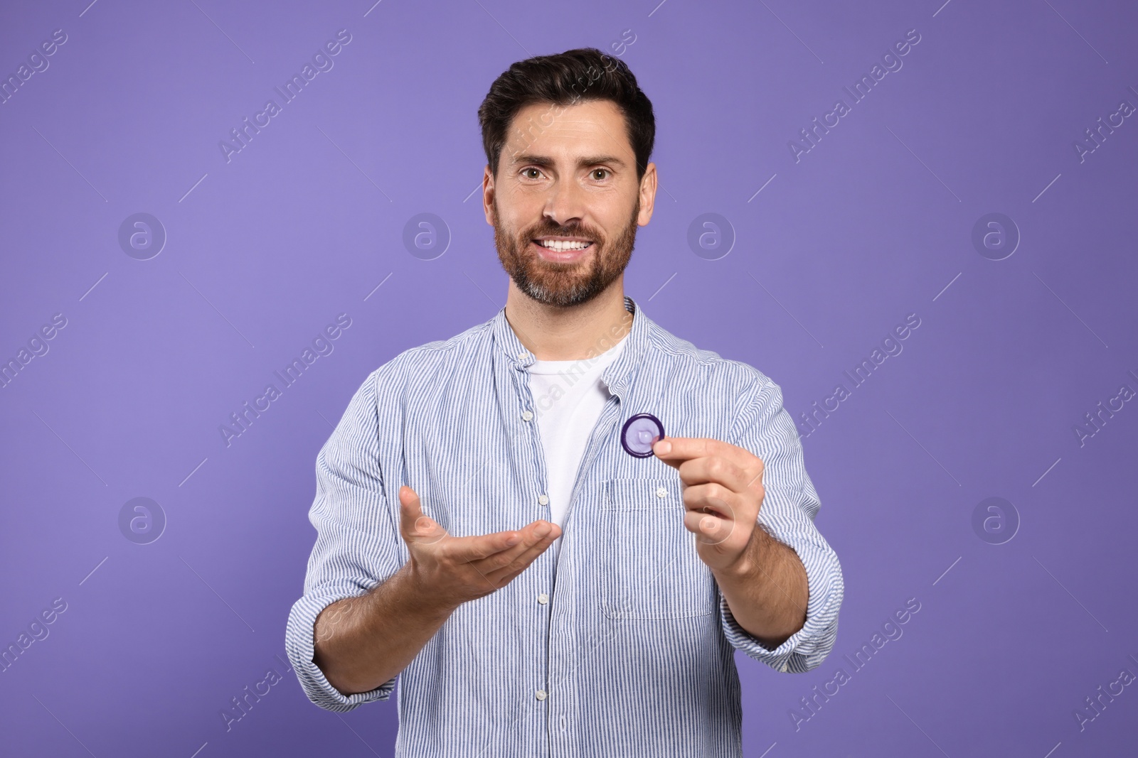 Photo of Man holding condom on purple background. Safe sex