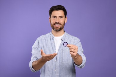 Man holding condom on purple background. Safe sex