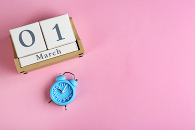 Photo of Wooden block calendar and alarm clock on pink background, flat lay. Space for text