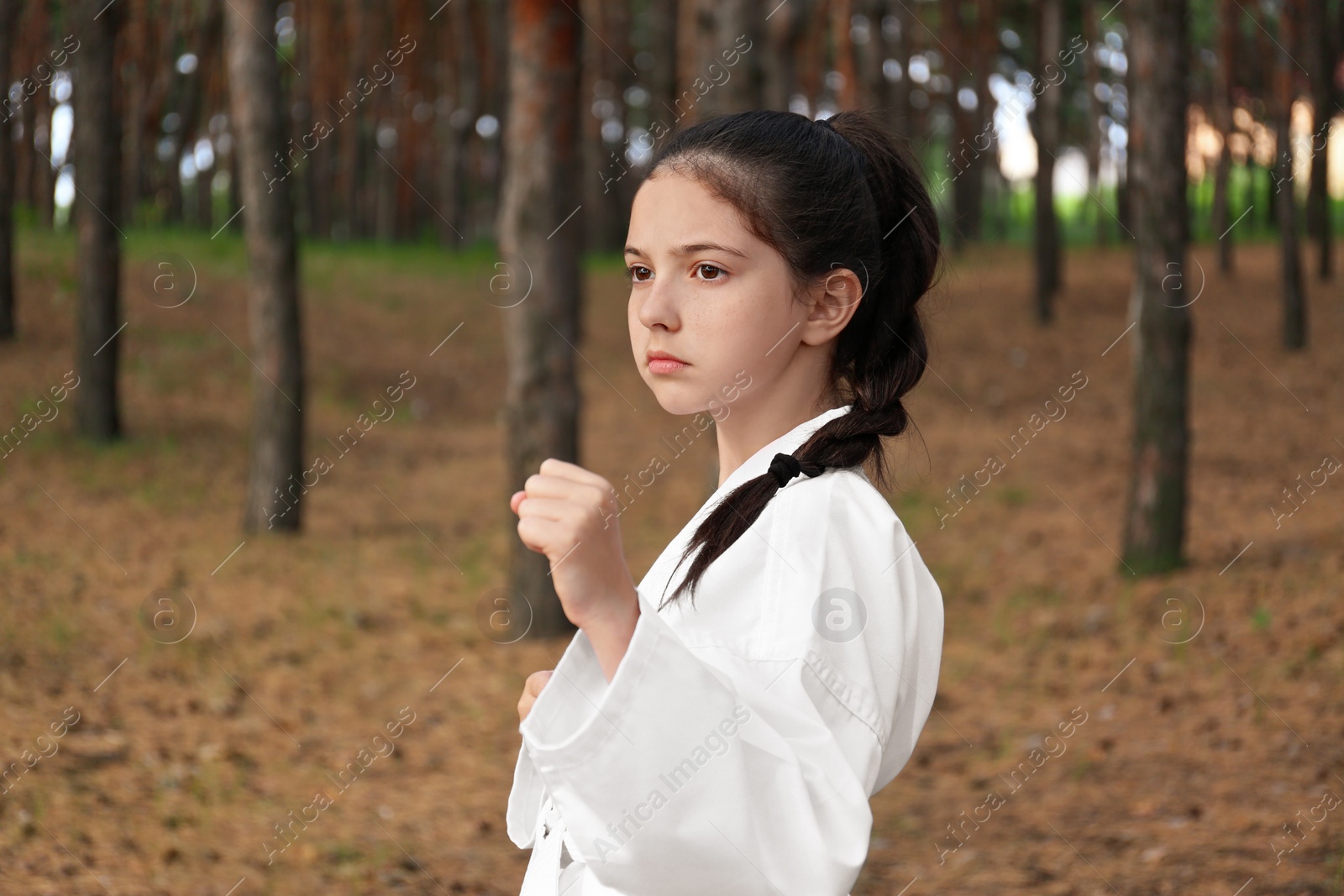 Photo of Cute little girl in kimono practicing karate in forest