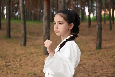 Cute little girl in kimono practicing karate in forest