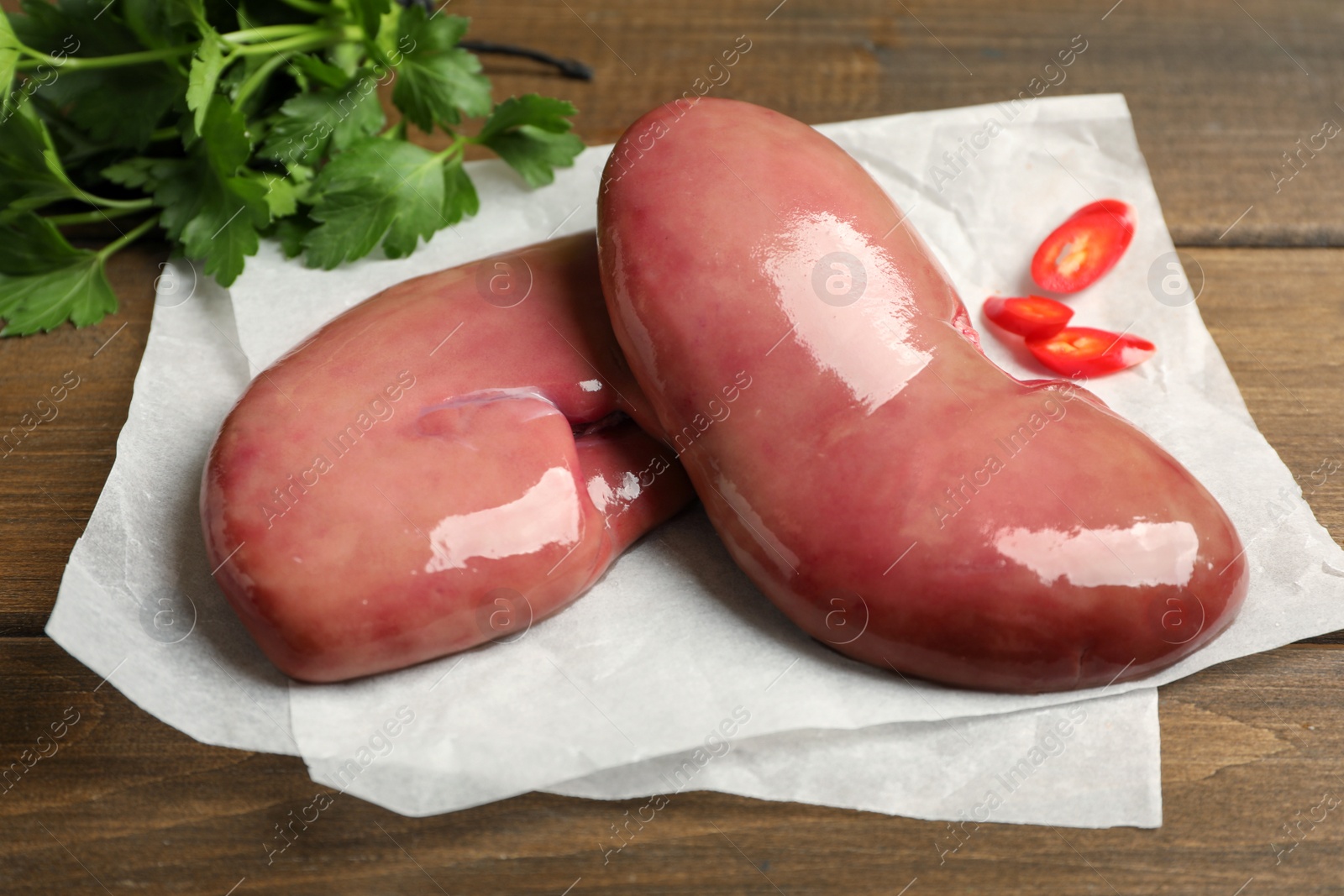Photo of Fresh raw pork kidneys on wooden table, closeup