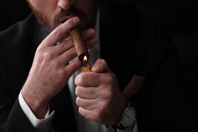 Photo of Man lightning cigar on black background, closeup