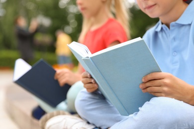Photo of Little children reading books outdoors, closeup