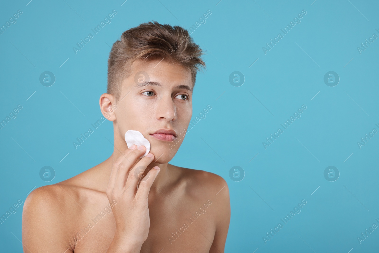 Photo of Handsome man cleaning face with cotton pad on light blue background, space for text