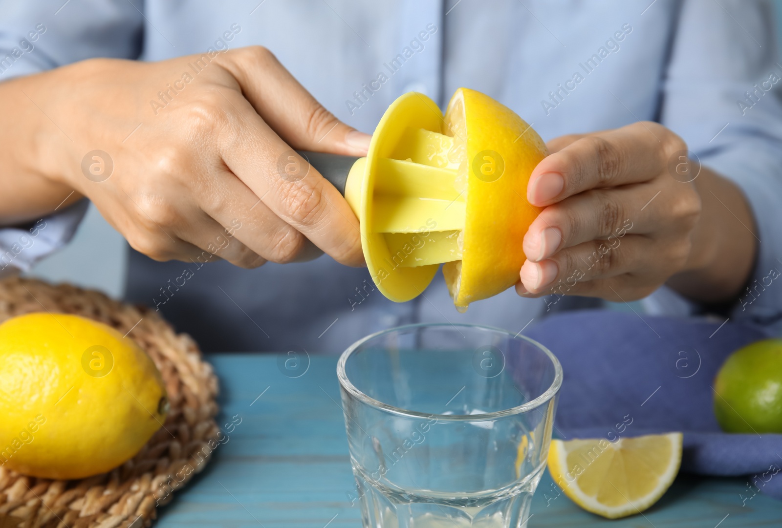 Photo of Woman squeezing lemon juice with citrus reamer at light blue wooden table, closeup