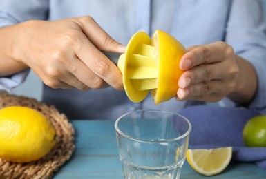 Woman squeezing lemon juice with citrus reamer at light blue wooden table, closeup