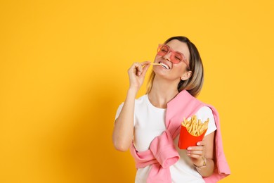 Young woman eating French fries on yellow background, space for text