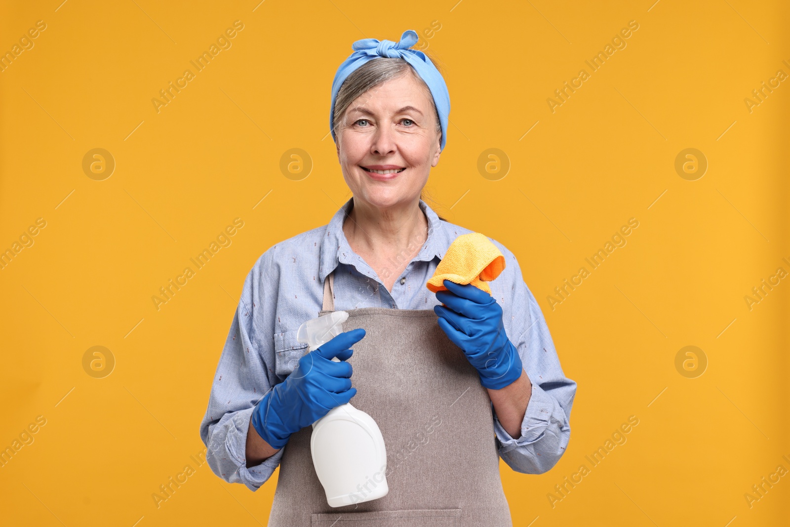 Photo of Happy housewife with spray bottle and rag on orange background