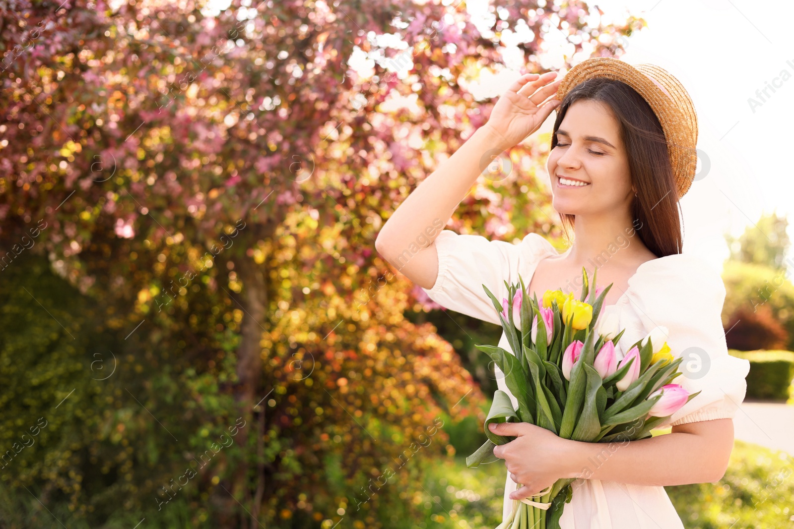 Photo of Beautiful young woman with bouquet of tulips in park on sunny day, space for text