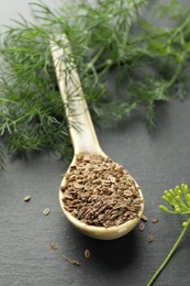 Photo of Spoon with dry seeds and fresh dill on black table, selective focus. Space for text