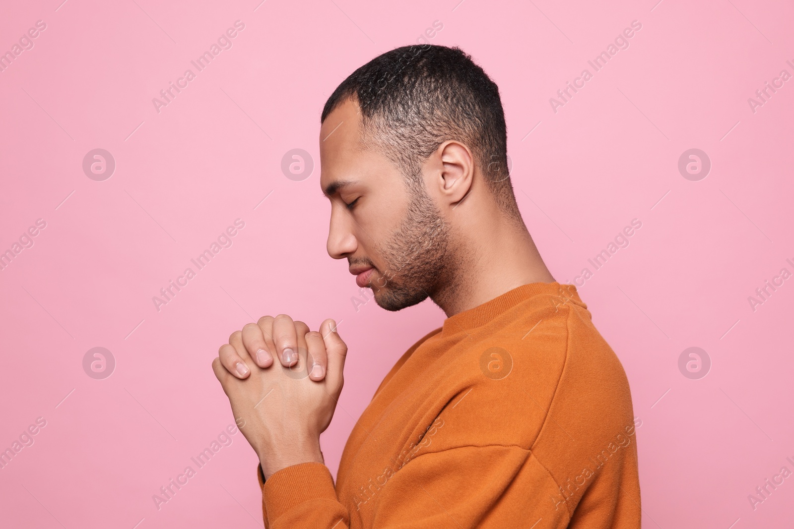 Photo of African American man with clasped hands praying to God on pink background