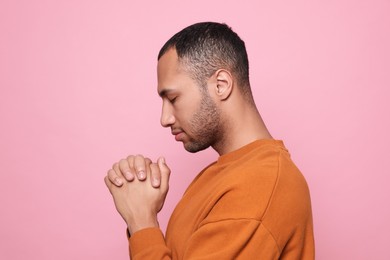 African American man with clasped hands praying to God on pink background