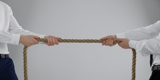 Dispute concept. Men pulling rope on light grey background, closeup. Space for text