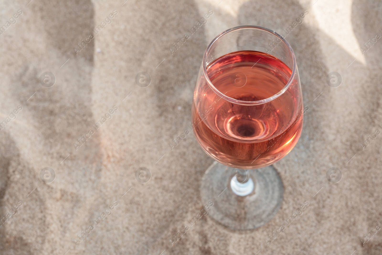 Photo of Glass of tasty rose wine on sand, above view. Space for text