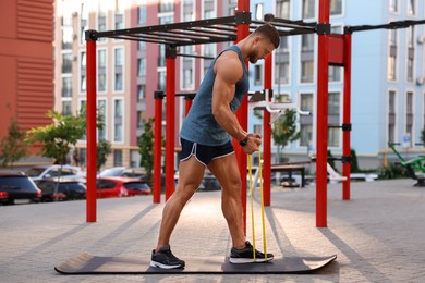 Photo of Muscular man doing exercise with elastic resistance band on mat at sports ground