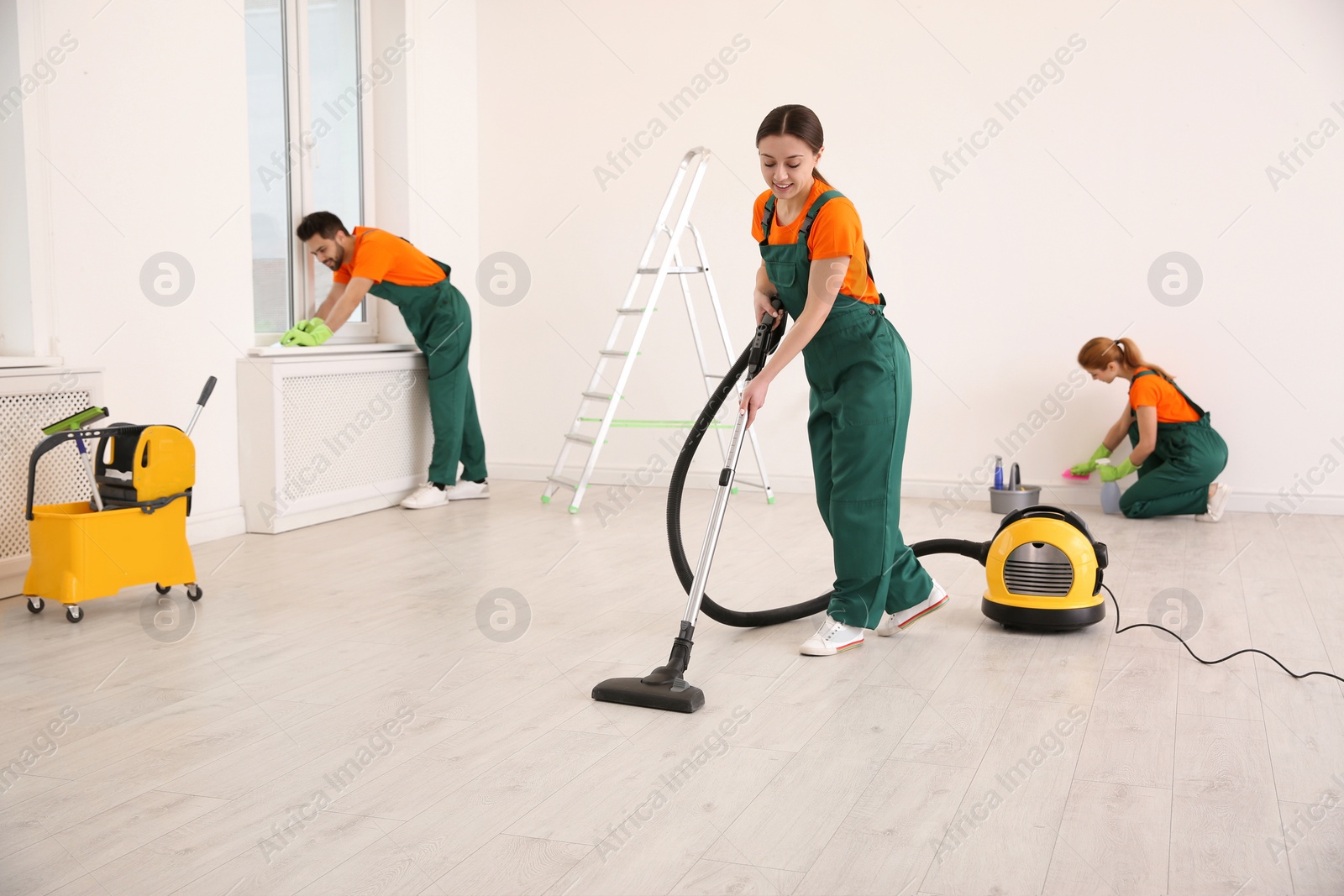 Photo of Team of professional janitors in uniforms cleaning room