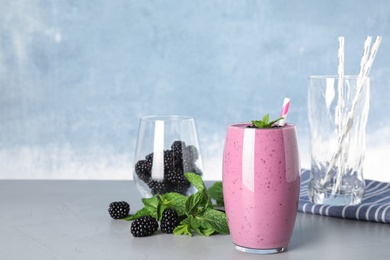 Glass of tasty blackberry smoothie and ingredients on grey table. Space for text