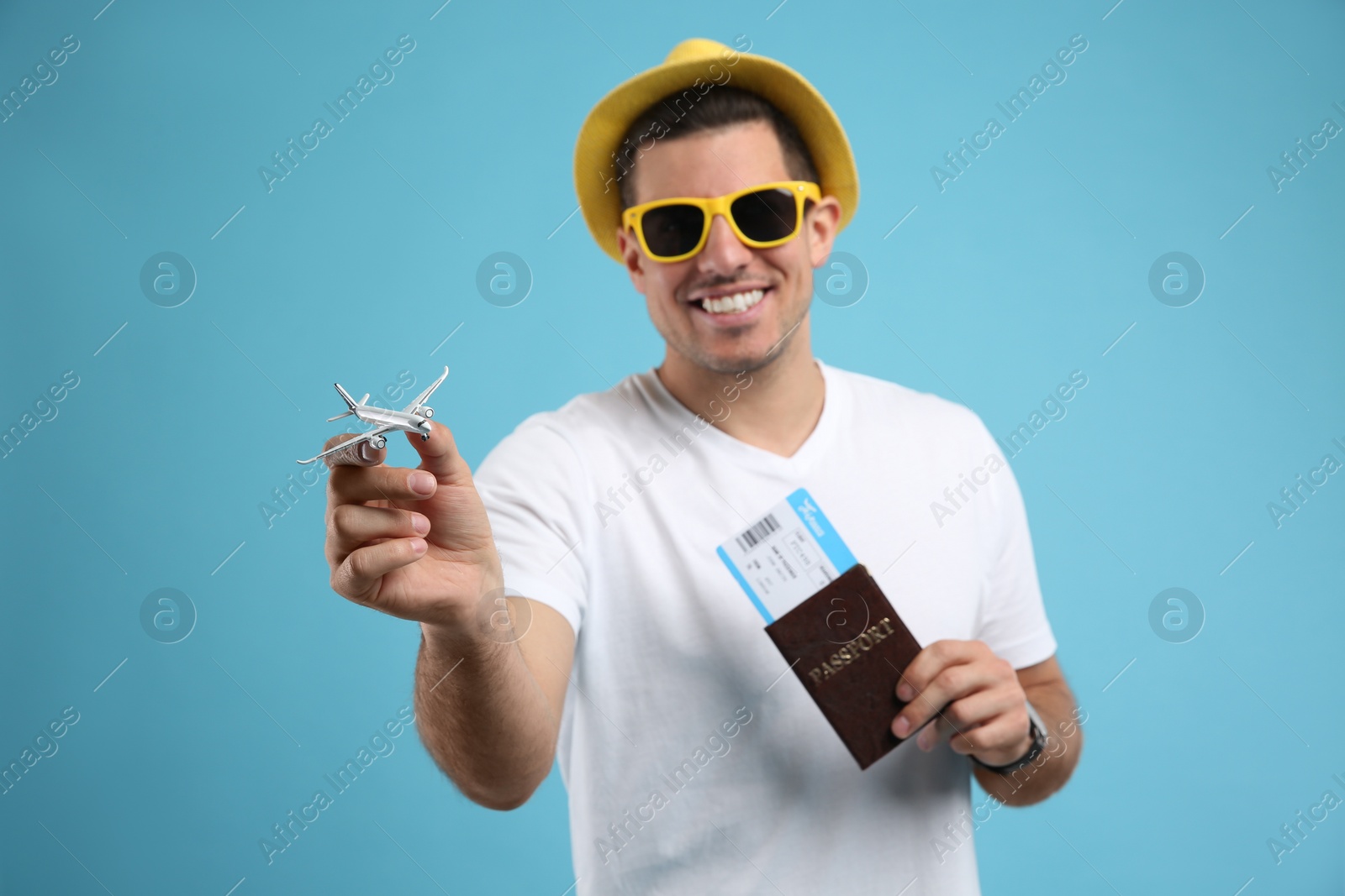 Photo of Male tourist holding passport with ticket against turquoise background, focus on toy airplane