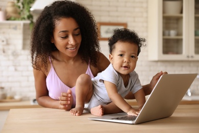 Photo of African-American woman and her baby with laptop in kitchen. Happiness of motherhood