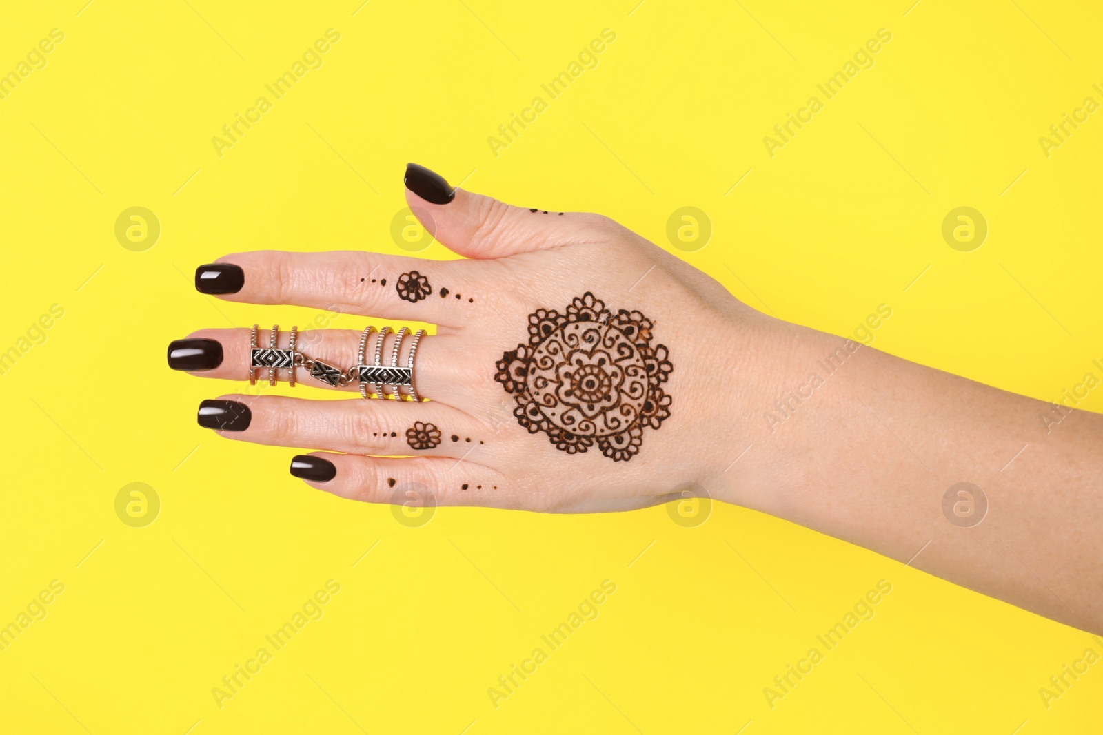 Photo of Woman with henna tattoo on hand against yellow background, closeup. Traditional mehndi ornament