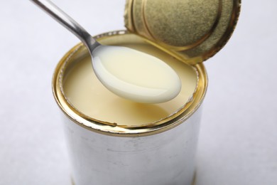 Photo of Spoon with condensed milk over open tin can on white table, closeup