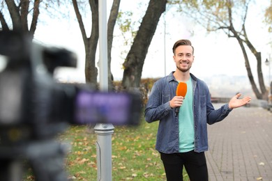 Young male journalist with microphone working in park