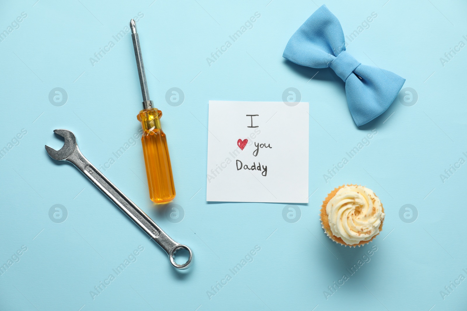 Photo of Card with phrase I Love You Daddy, cupcake and men accessories on light blue background, flat lay. Father's day celebration