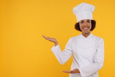 Photo of Portrait of happy female chef in uniform on orange background. Space for text