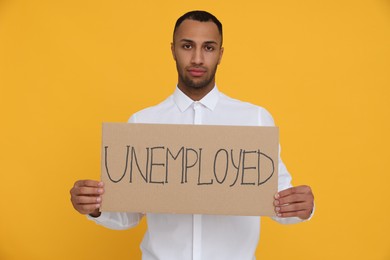 Photo of Young man holding sign with word Unemployed on yellow background