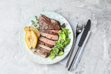 Photo of Delicious roasted beef meat served with caramelized pear and greens on light textured table, top view