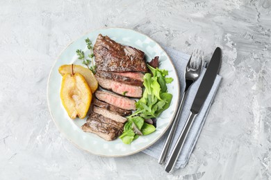 Delicious roasted beef meat served with caramelized pear and greens on light textured table, top view