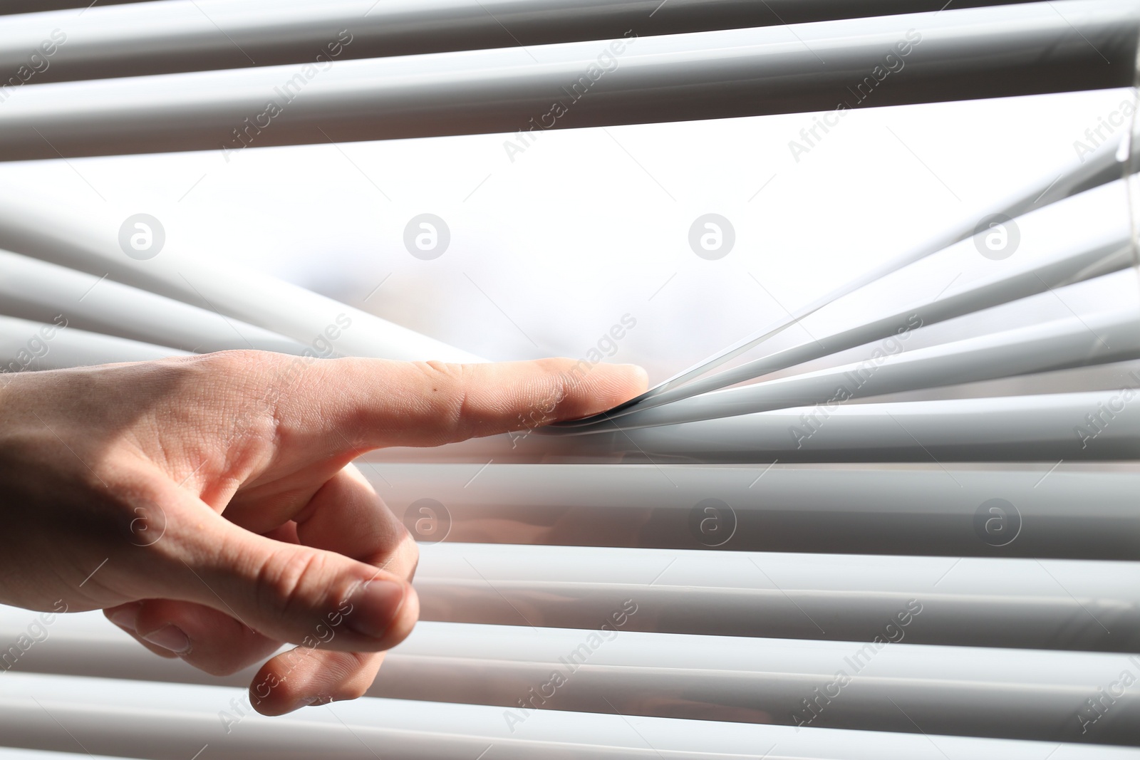 Photo of Man separating slats of white blinds indoors, closeup