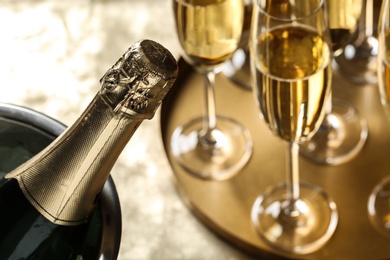 Photo of Bottle of champagne in bucket with ice and glasses on table, closeup. Space for text