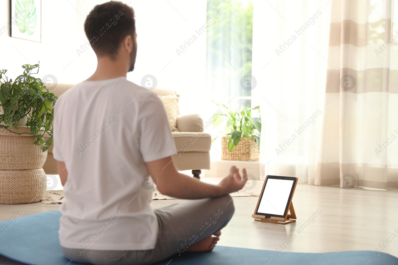 Photo of Man practicing yoga while watching online class at home during coronavirus pandemic. Social distancing