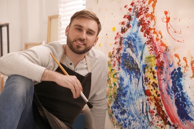 Photo of Young man with painting brush near canvas in artist studio