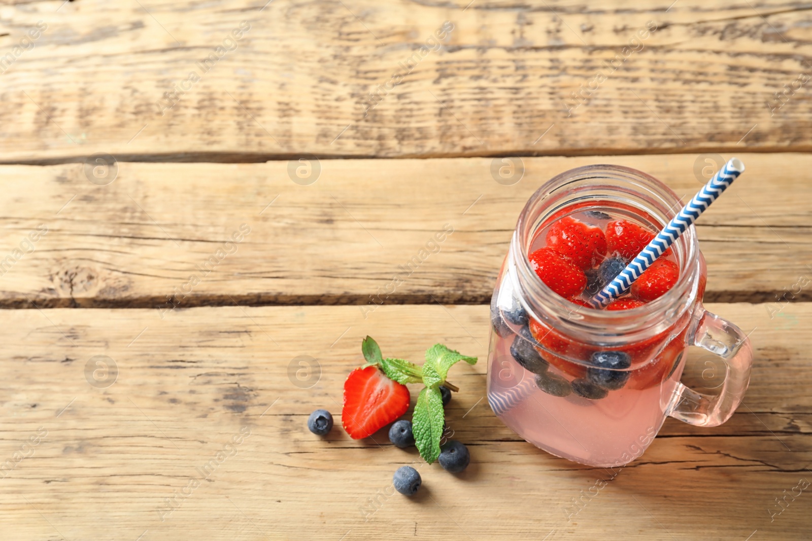 Photo of Natural lemonade with berries in mason jar on wooden table