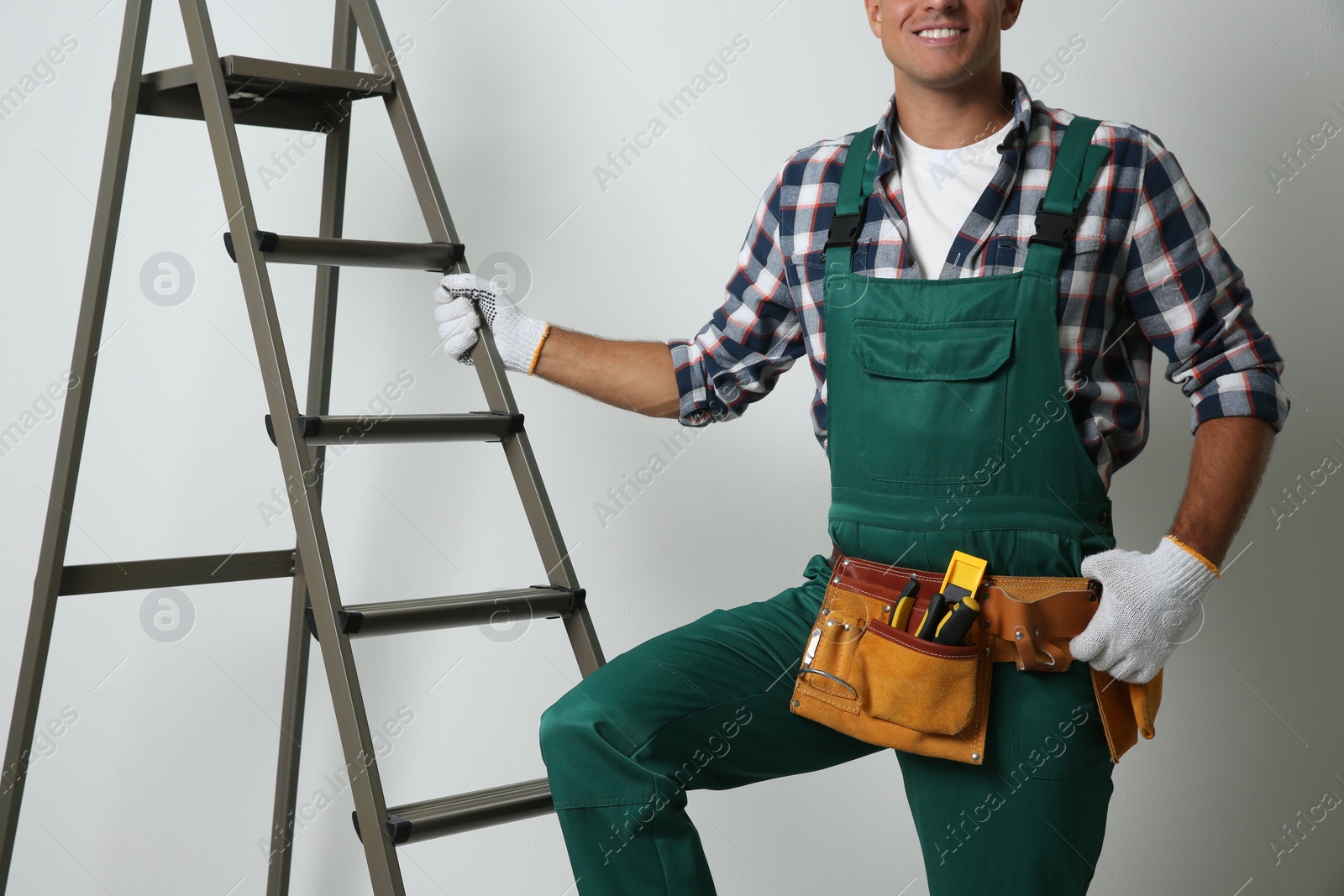 Photo of Professional builder near metal ladder on light background, closeup