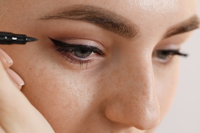 Photo of Makeup product. Woman applying black eyeliner on blurred background, closeup