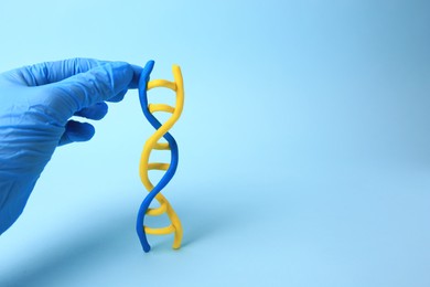 Photo of Scientist with DNA molecule model made of plasticine on light blue background, closeup. Space for text