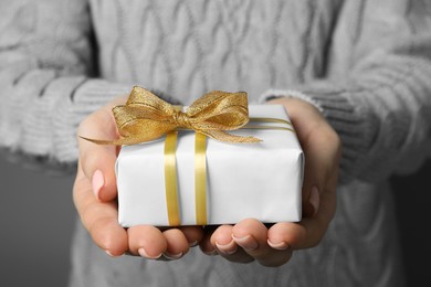 Christmas present. Woman holding gift box against grey background, closeup